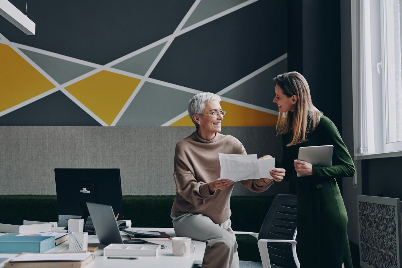 two confident women discussing business and smiling while working in the office together Business Coaching